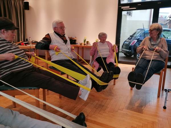Kunden der Diakoniestation bei der Gymnastik mit Dehnbändern auf Stühlen sitzend